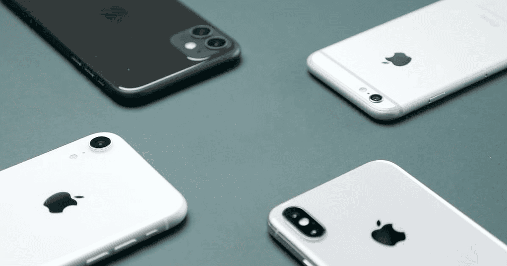 Four iPhones over a green-gray surface, facing each other from the top side